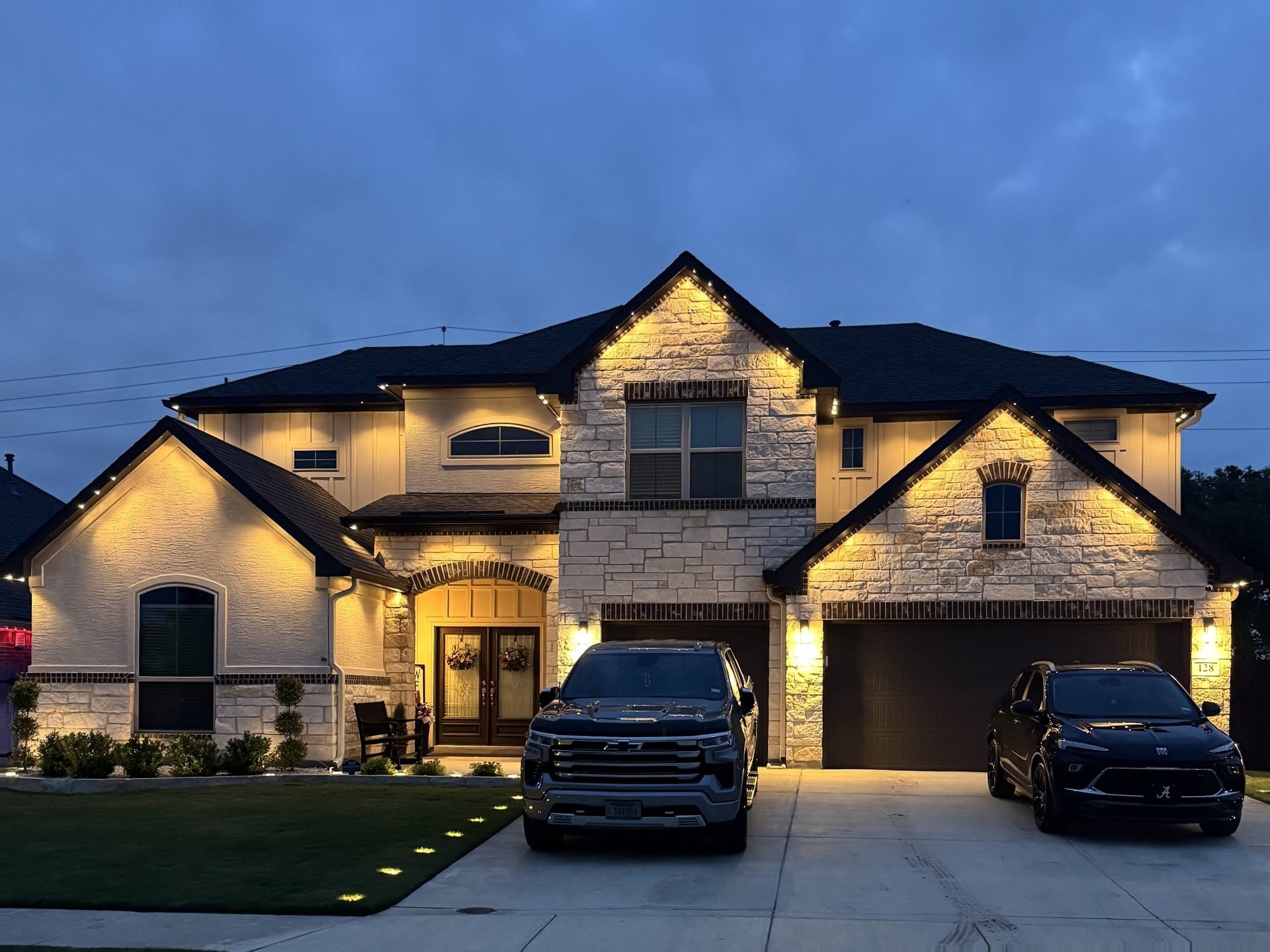 White-stucco and stone Texas home with warm white permanent LED roofline lighting at dusk