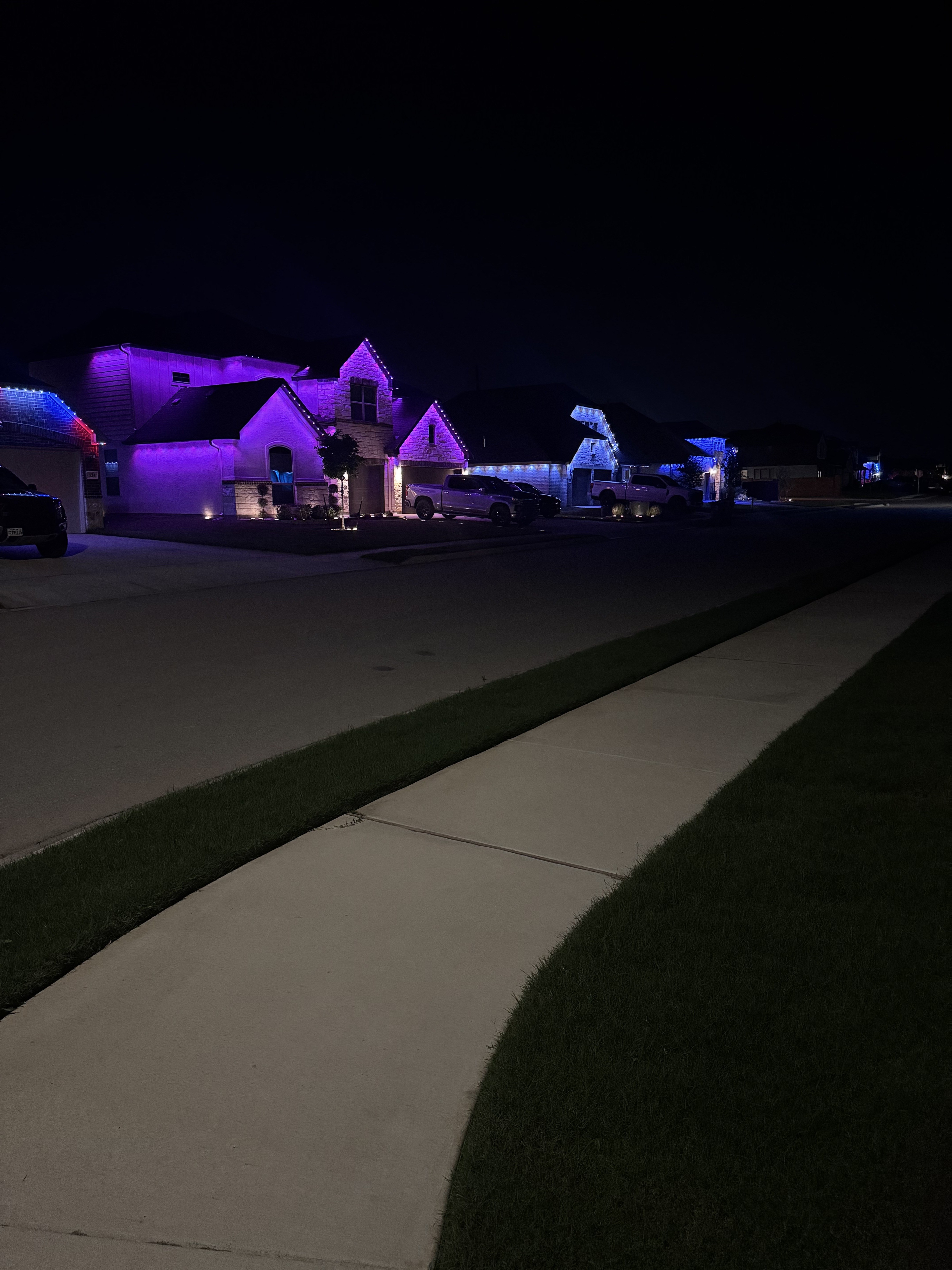 Texas neighborhood street view with multiple homes lit up by Dazzl permanent LED lighting at night